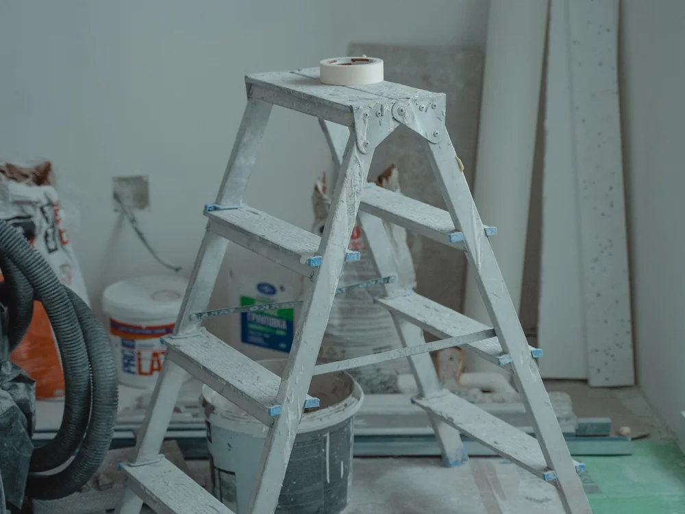 Pièce vide préparée avant peinture, escabeau et sol protégé par une bâche.